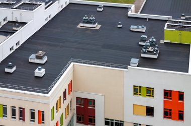 Top view flat roof with air conditioners and hydro insulation membranes on top of a modern apartment yellow green red building.